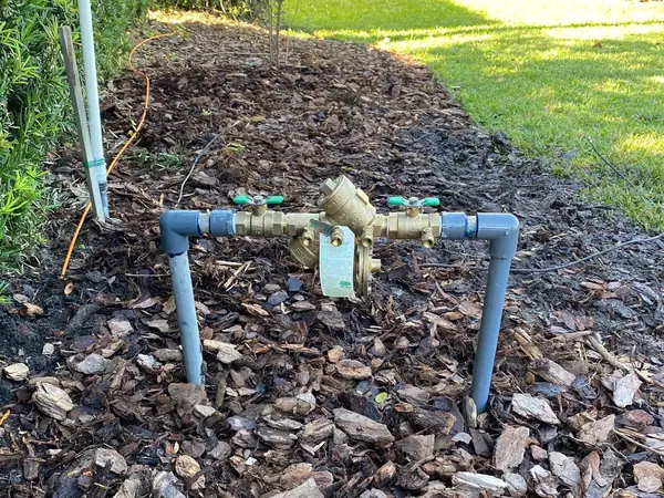 New irrigation backflow preventer on blue risers in a pine-bark mulch bed beside a lawn