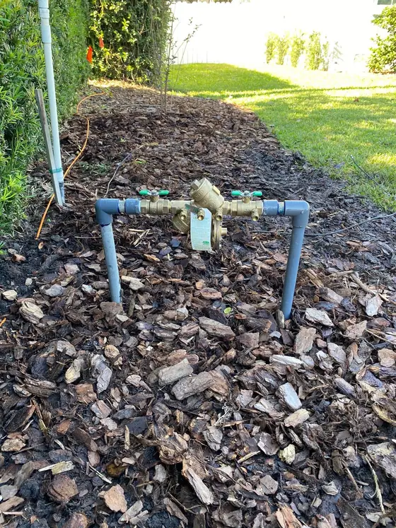 Brass backflow preventer installed on an irrigation line in a mulched side bed
