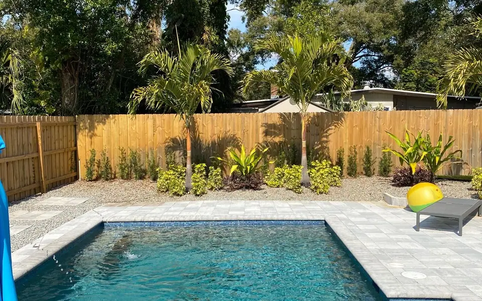 Pool landscape with palms, shrubs and paver deck inside a wood privacy fence