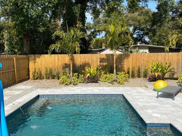 Paver pool deck with palms and shrubs planted along a wood fence
